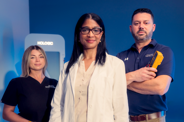 Tres profesionales sanitarios posando frente a un equipo médico de Hologic