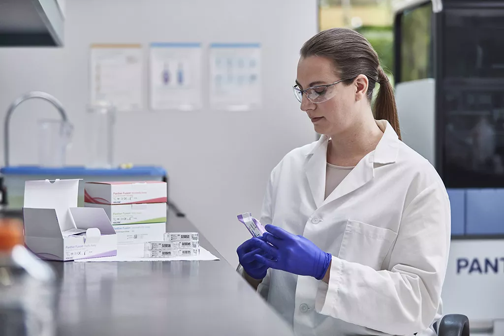 Técnico de laboratorio con varias cajas de ensayos y laboratorio al fondo