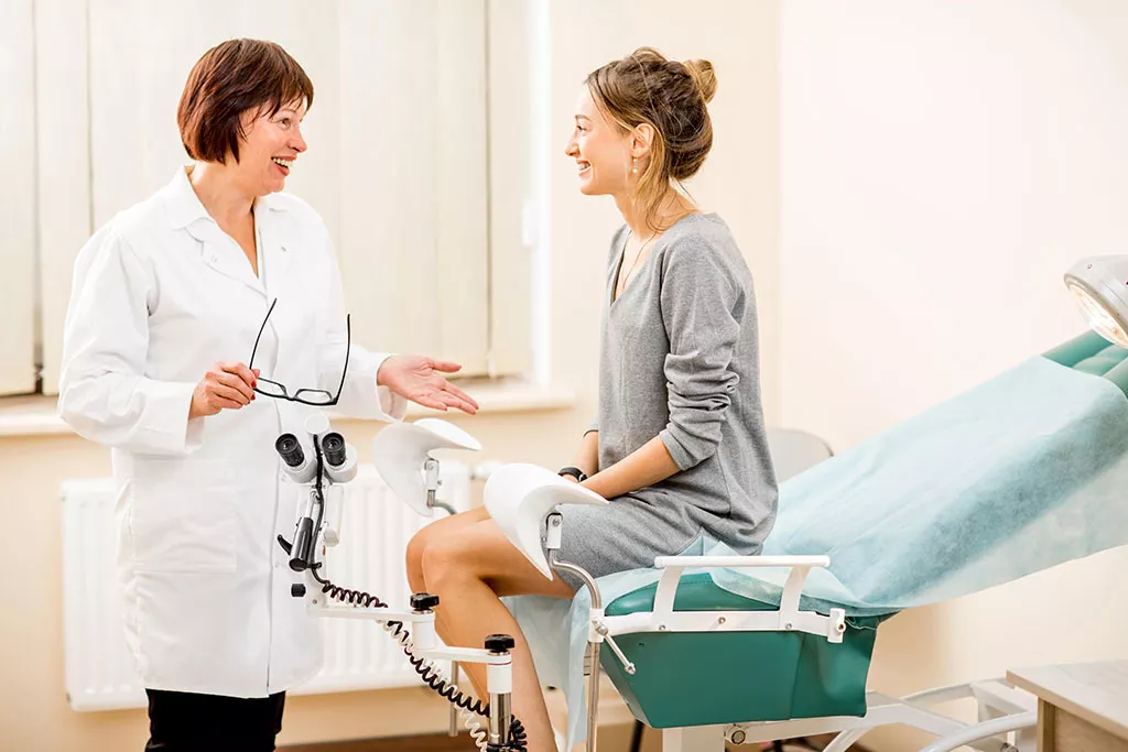 Paciente sentada en una camilla de exploración de un hospital conversando con un profesional sanitario