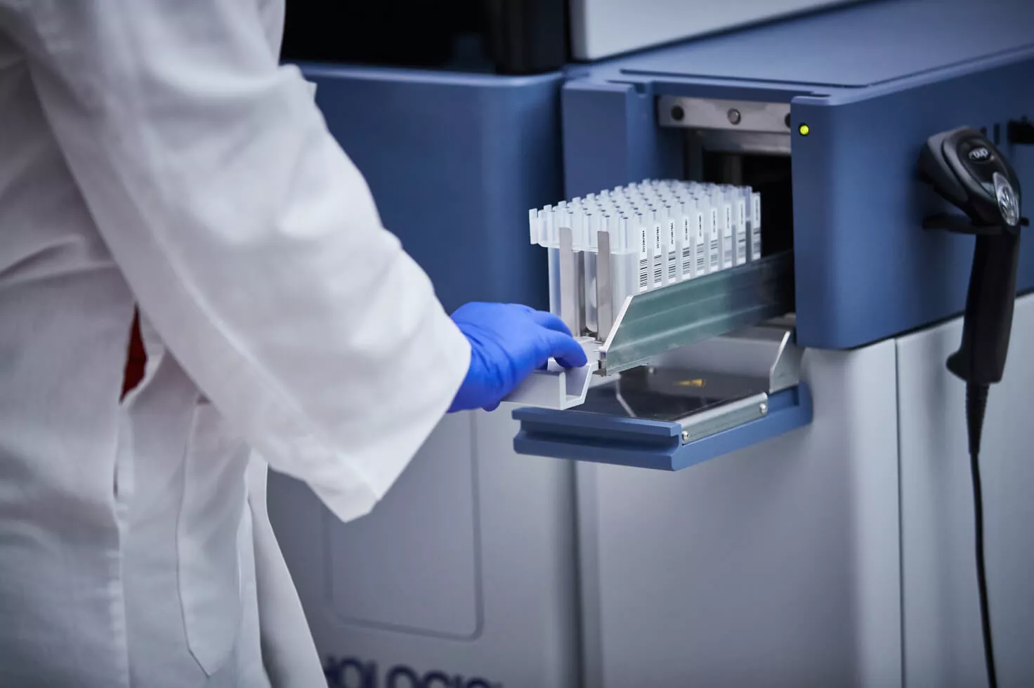 Técnico de laboratorio que empuja una bandeja de viales para introducirla en un equipo médico